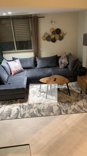 Ein Wohnzimmer mit einem grauen Ecksofa, einem Holztisch und einem Teppich mit Muster.