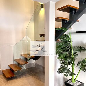 Eine moderne Treppe mit Glastrennläufen und Holzstufen, die zu einer Zwischenebene mit einer Holzplattform führt.