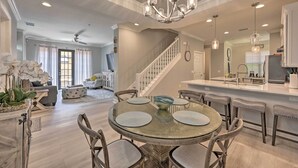 A spacious living area with a round dining table, a chandelier, and a staircase leading to another level.