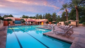 A swimming pool with lounge chairs and umbrellas, surrounded by palm trees and buildings. - Club Wyndham Orange Tree Resort (Scottsdale)