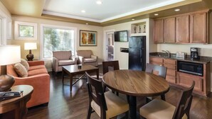 A modern living room with a sofa, coffee table, and dining table. There is a kitchen area with cabinets and appliances. - Club Wyndham Orange Tree Resort (Scottsdale)