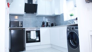 Una cucina moderna con mobili bianchi, forno a microonde integrato, macchina da caffè, forno e lavatrice.