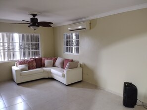 A living room with a white sectional sofa, a ceiling fan, and an air conditioning unit.