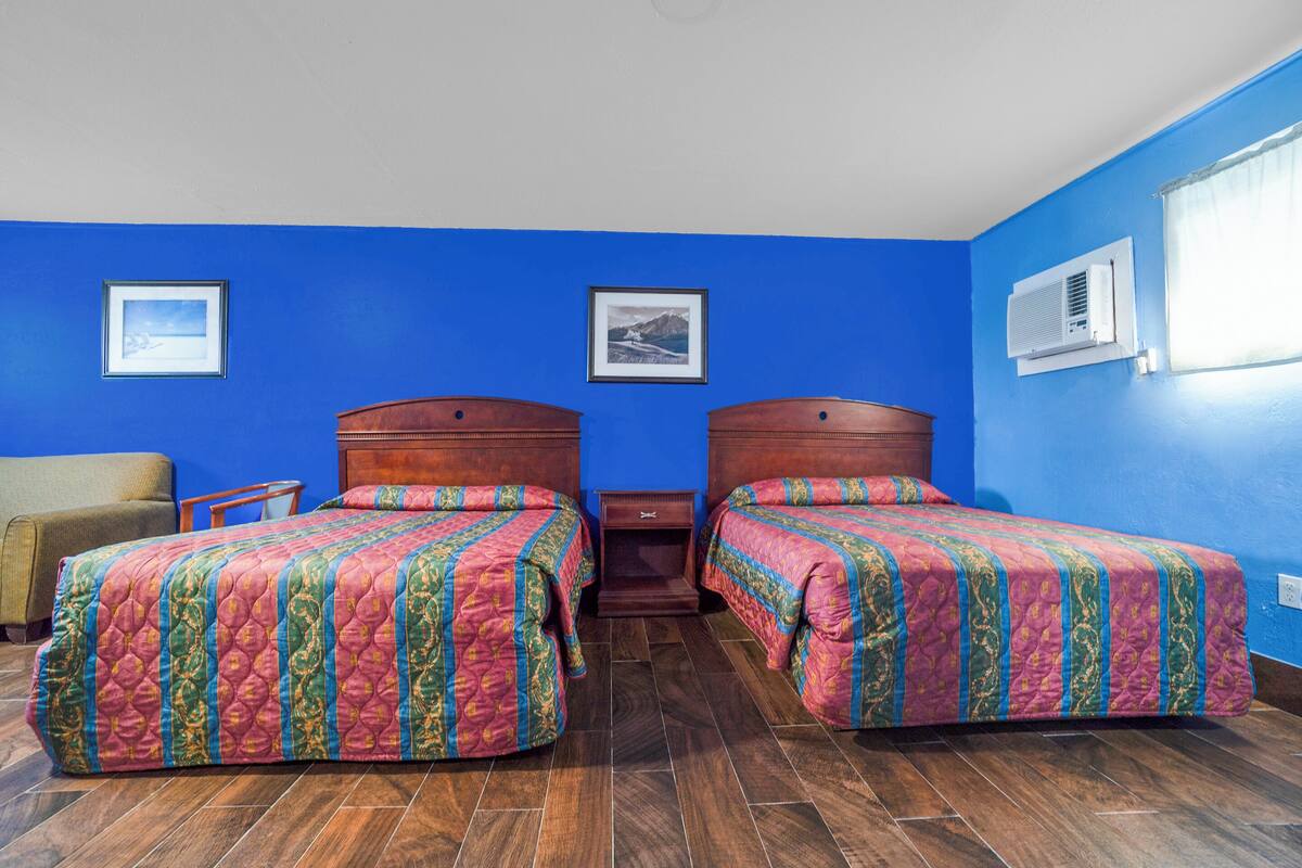 Una habitación con dos camas, cabecero de madera, una mesita pequeña y dos cuadros enmarcados en la pared.
