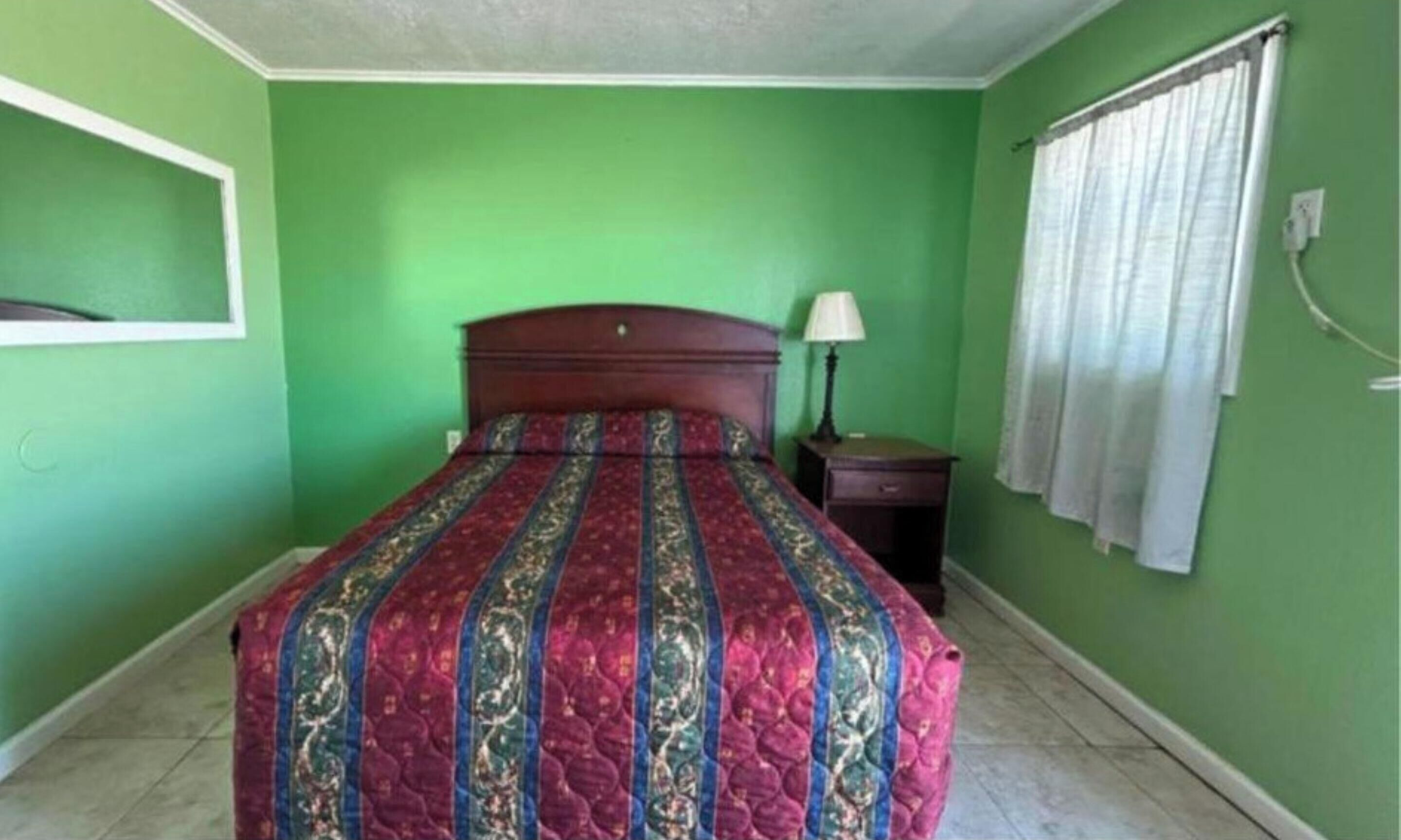 A bedroom with a bed, a nightstand, a lamp, and a window with curtains.