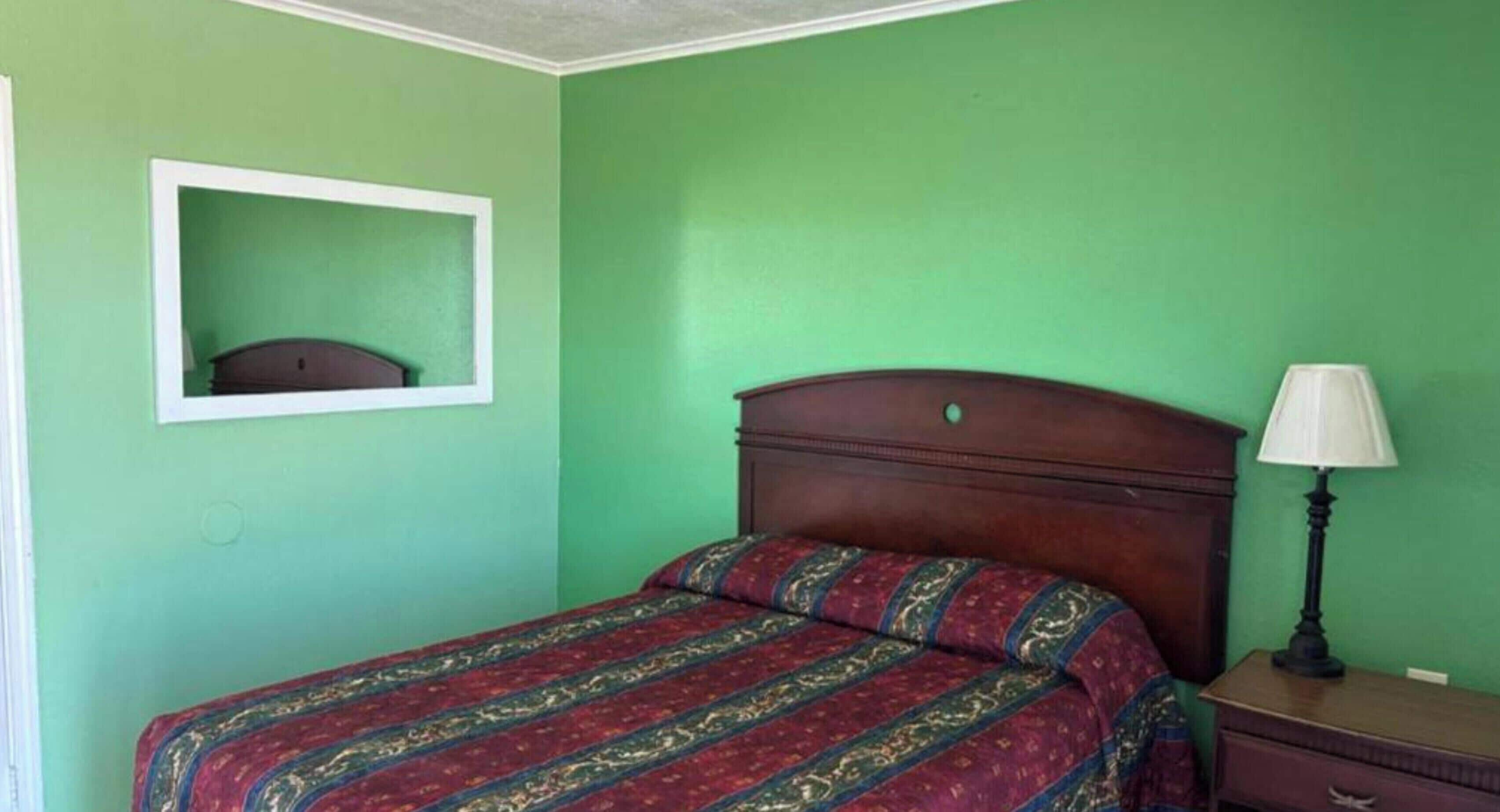 Ein Einzelbett mit gemustertem Überwurf, ein Nachttisch mit Lampe und ein gerahmter Spiegel an der Wand.