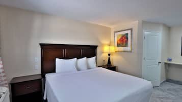 A hotel room with a bed, a nightstand, a lamp, a door, and a painting on the wall.