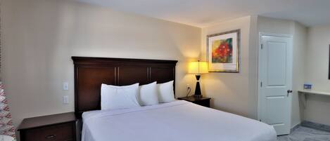 Une chambre d’hôtel avec un lit, une table de chevet, une lampe, une porte et un tableau au mur.