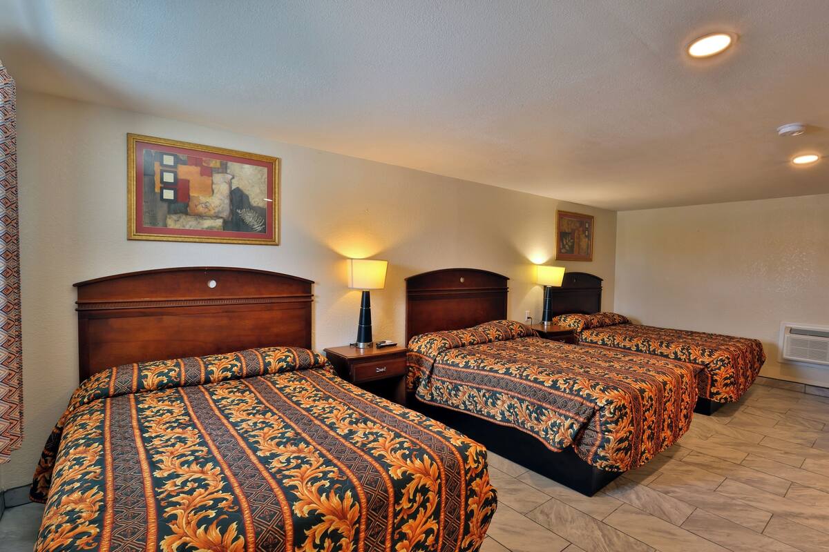 Habitación de hotel con tres camas, cabeceros de madera y un cuadro en la pared.