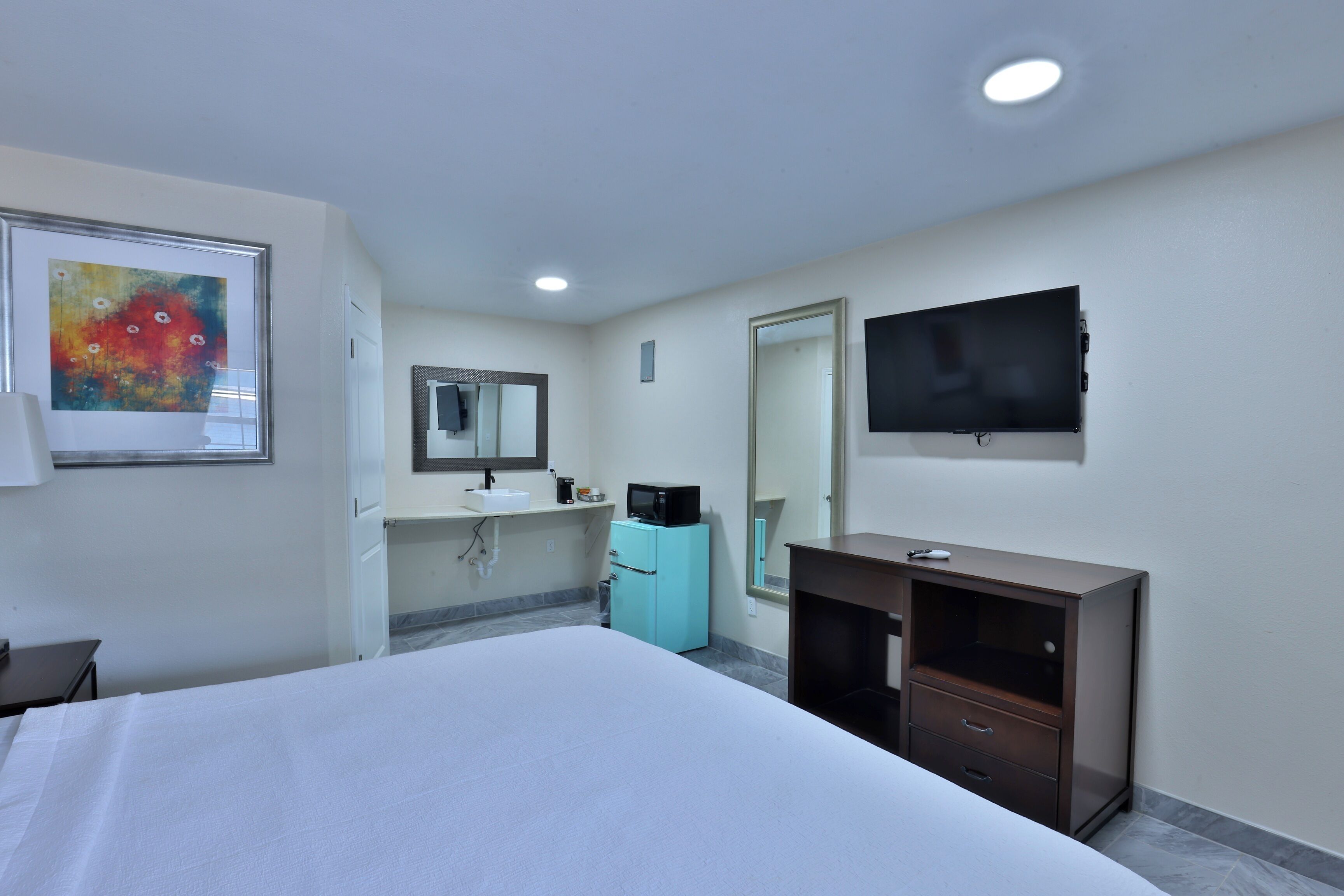 A hotel room with a bed, a sink, a mirror, a television, and a cabinet.