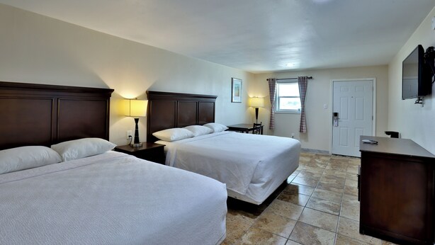 A hotel room with two beds, a desk, a chair, a TV, and a door. - Monterrey Motel Padre Island, Corpus Christi By Oyo (Corpus Christi)