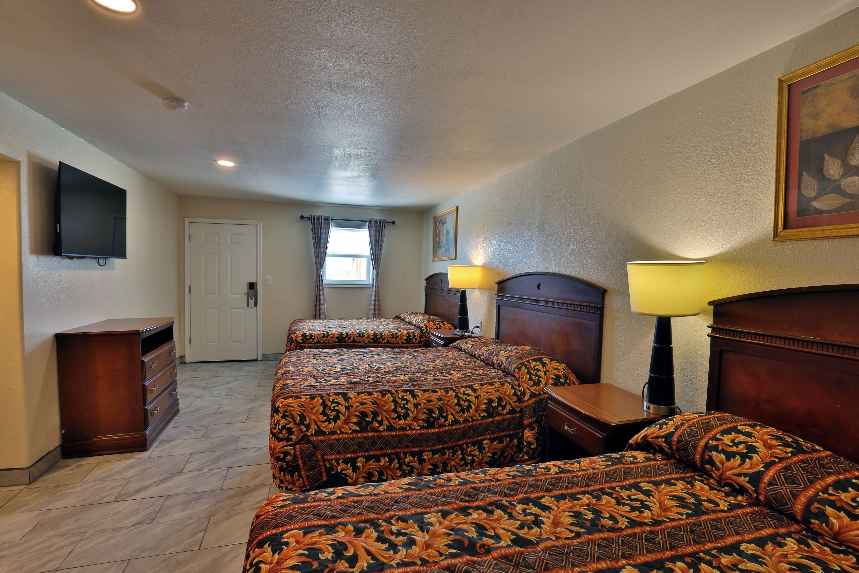 A hotel room with a large bed, a dresser, a television, and a window with curtains.