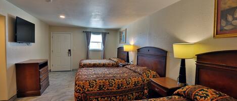 A hotel room with a large bed, a dresser, a television, and a window with curtains.