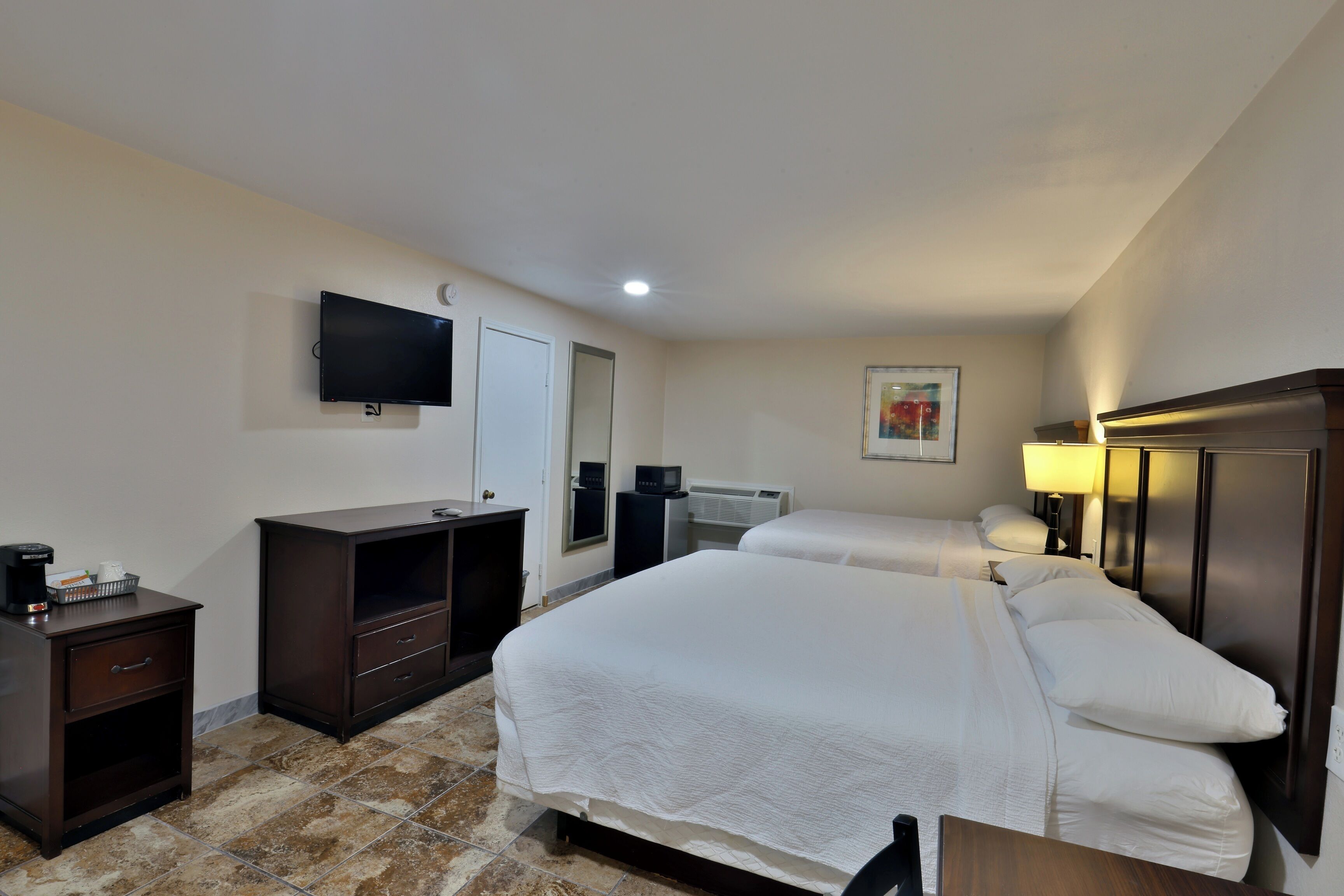 Habitación de hotel con dos camas, televisor, escritorio con cafetera y espejo.