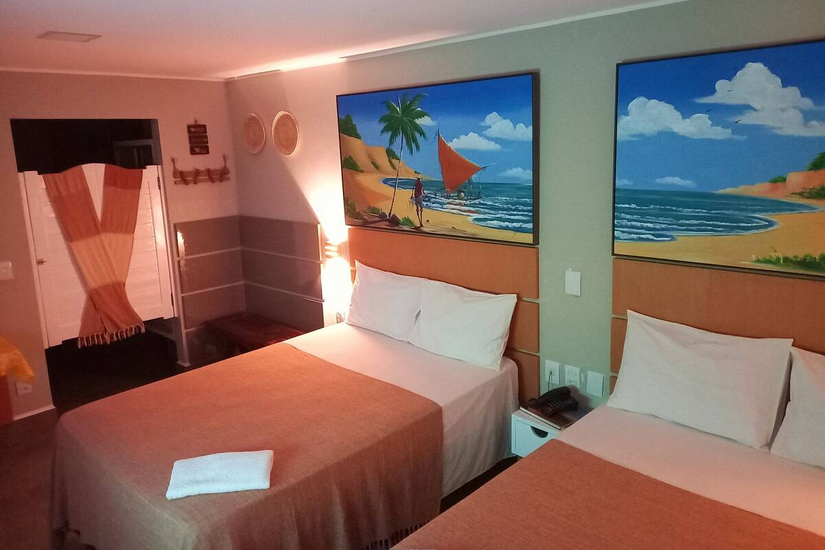 Habitación de hotel con dos camas, un cuadro de una playa, una puerta y un teléfono fijado a la pared.