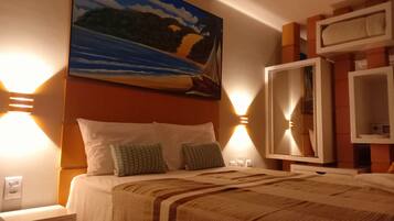 Habitación de hotel con una cama, dos almohadas, una manta, un cuadro en la pared y dos lámparas de pared.