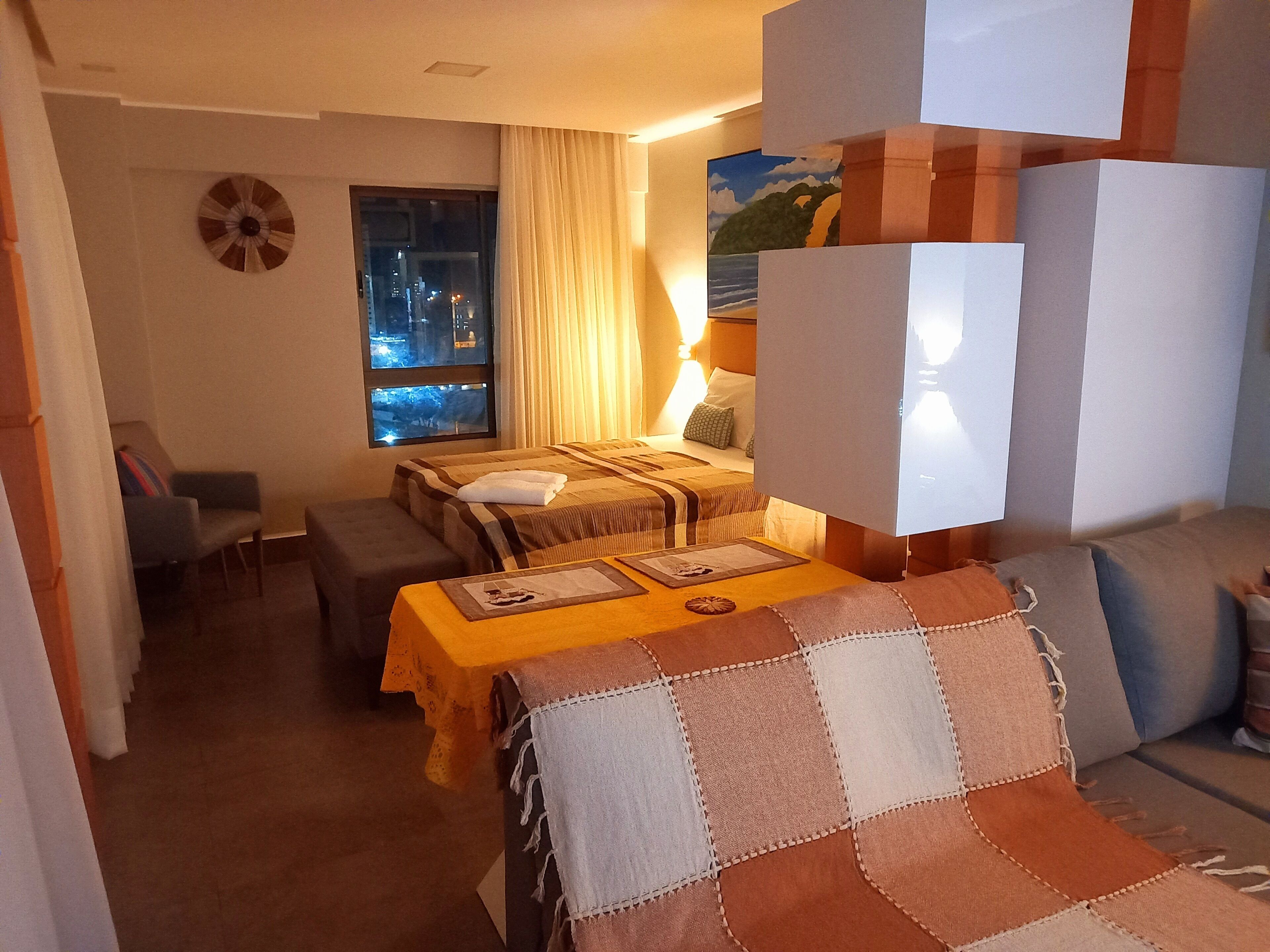 Quarto de hotel com duas camas, um sofá, uma mesinha e janela com vista para a cidade.