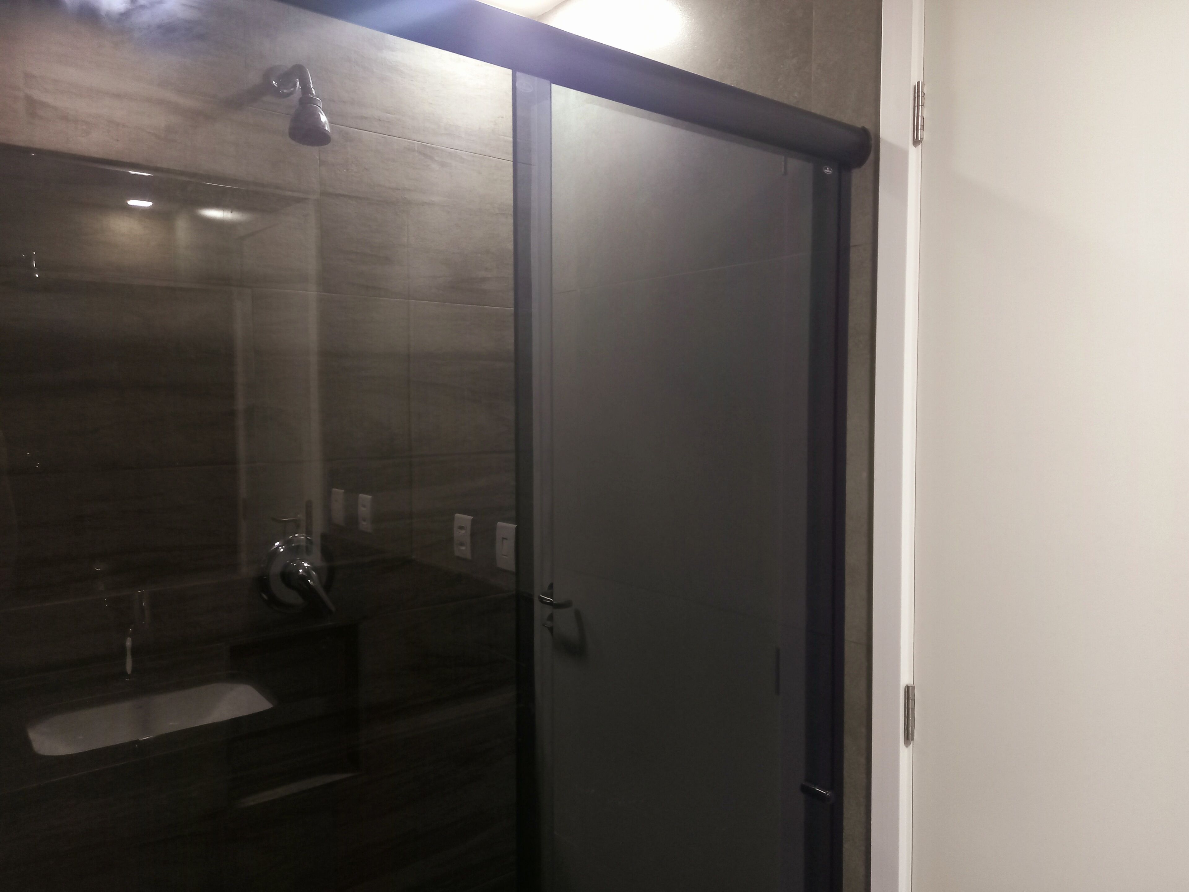 Um banheiro moderno com box de vidro, parede revestida de azulejos escuros e pia branca.