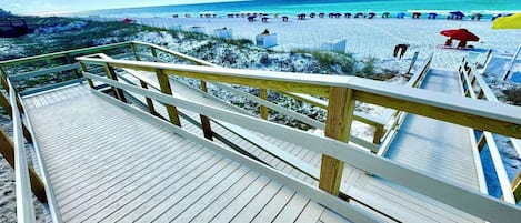 A wooden boardwalk leading to a beach with umbrellas and people.