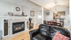 A living room with a fireplace, a black leather sofa, and a dining area with chairs and a table.