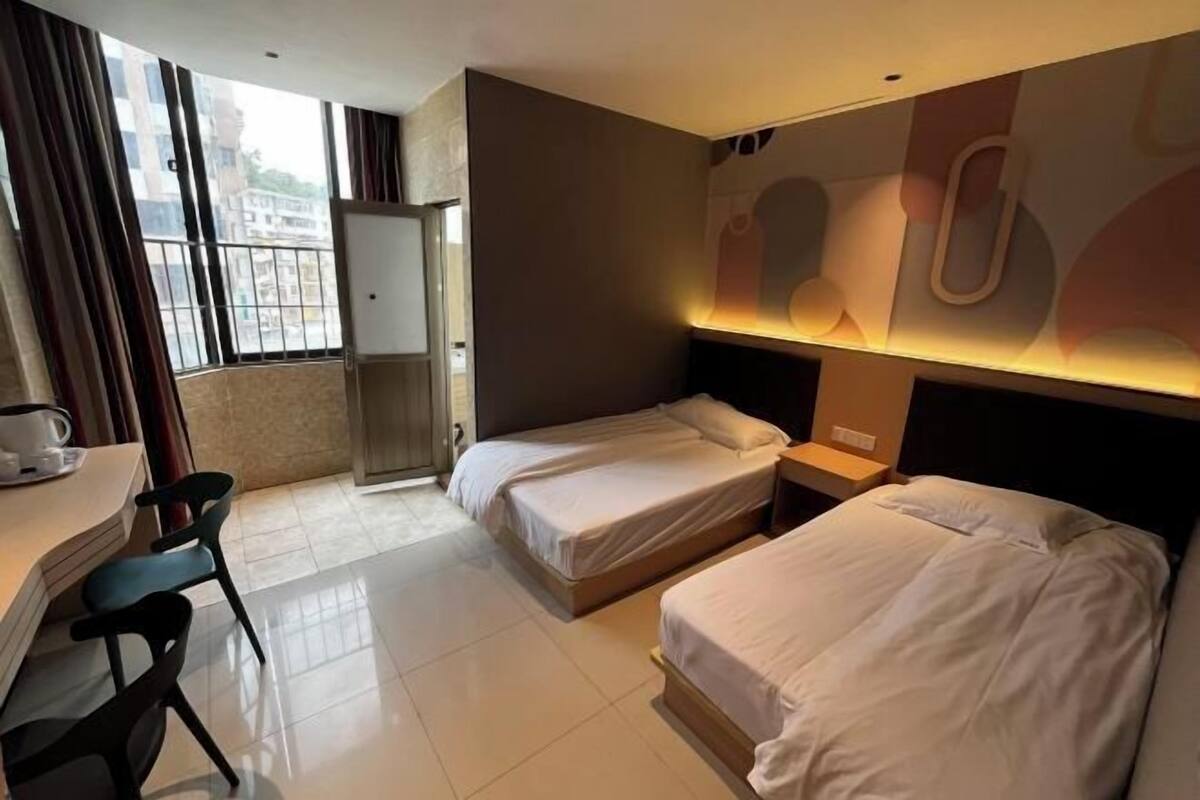 A hotel room with two beds, a desk with a chair, a small table, and a window with curtains.