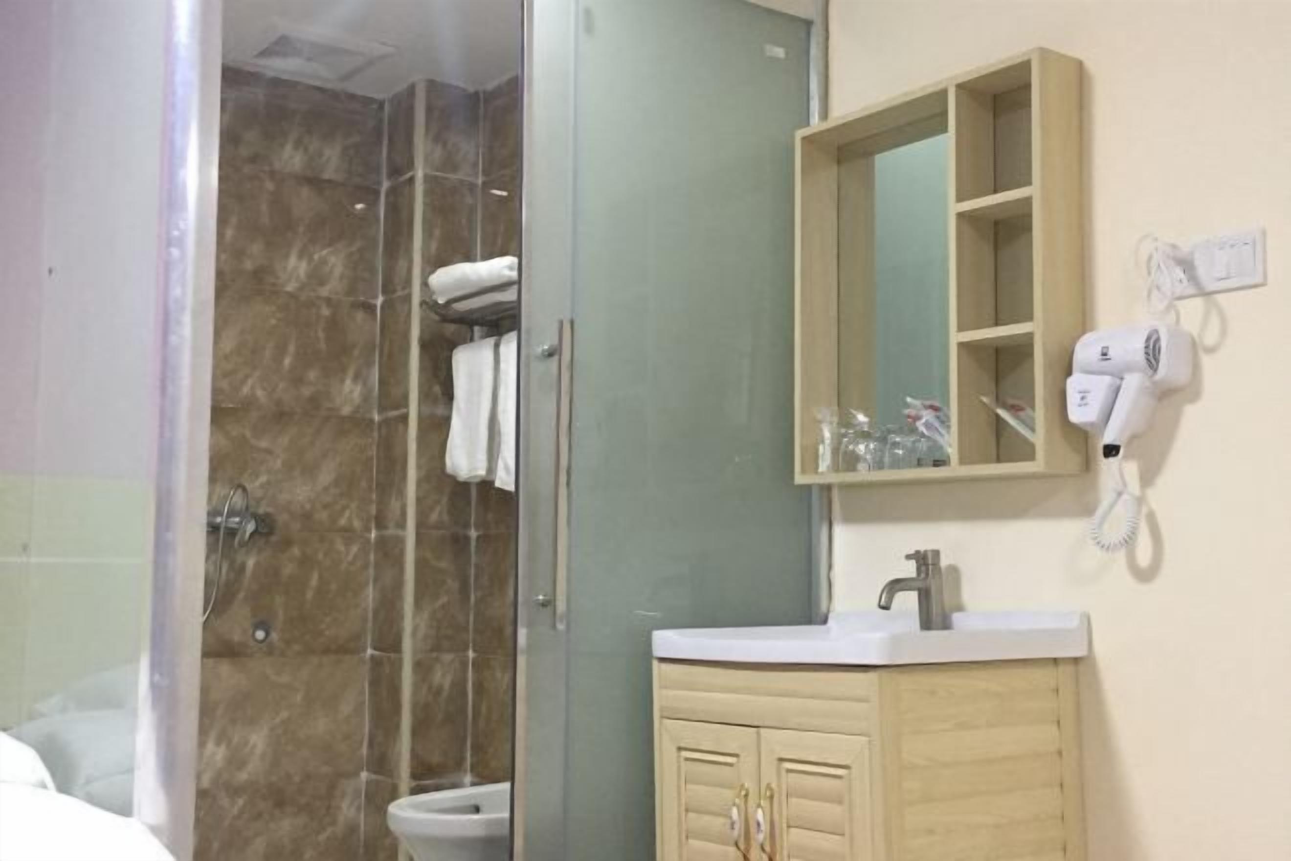 Un baño con cabina de ducha de vidrio, inodoro, lavabo con mueble de espejo y secador de pelo en la pared.
