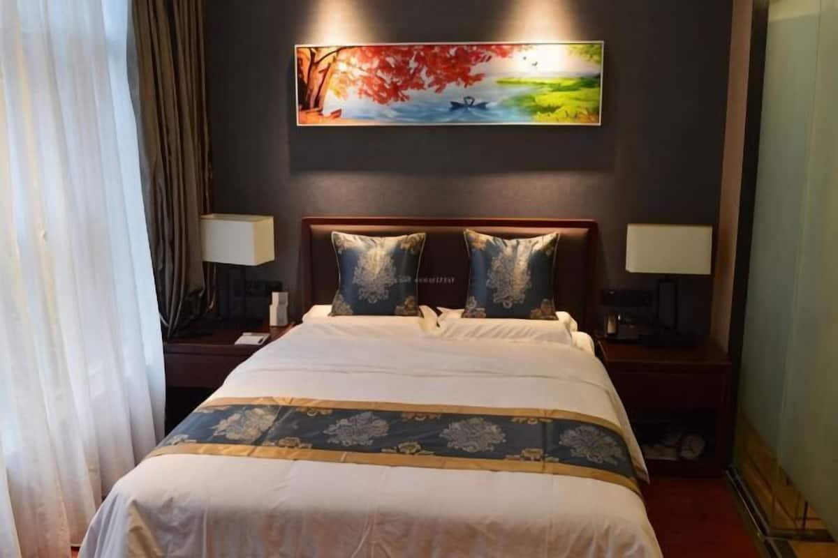 A hotel room with a large bed, two bedside tables with lamps, a painting on the wall, and a window with curtains.
