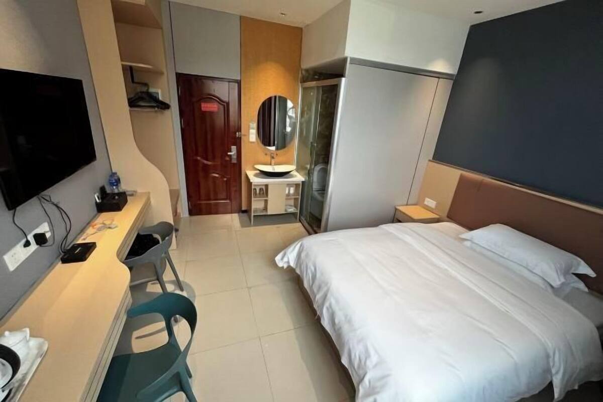 A hotel room with a bed, a desk with a chair, a TV, a mirror, and a wardrobe.