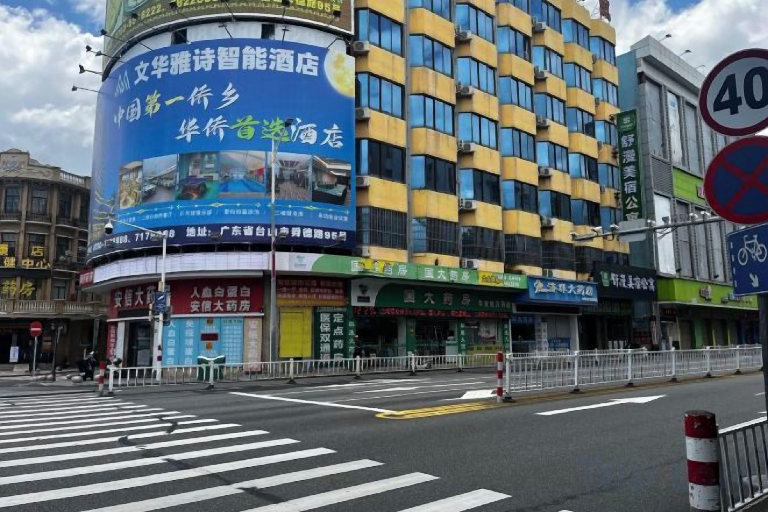 A multi-story building with a blue advertisement on the side, a pedestrian crossing, and a no parking sign.