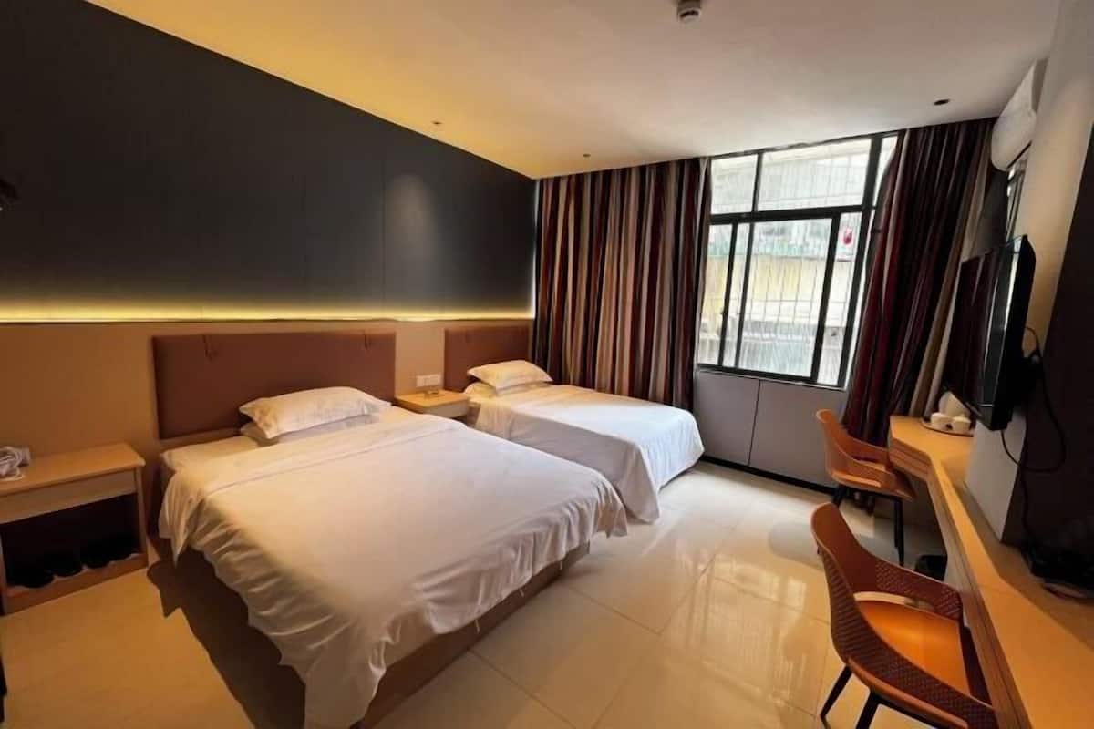 A hotel room with two beds, a desk, a chair, and a TV.