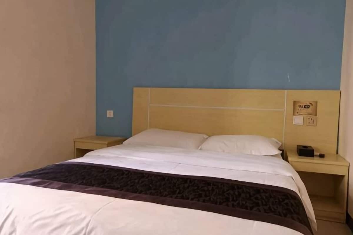 A single bed with a wooden headboard, a bedside table with a lamp, and a wall-mounted electrical outlet.