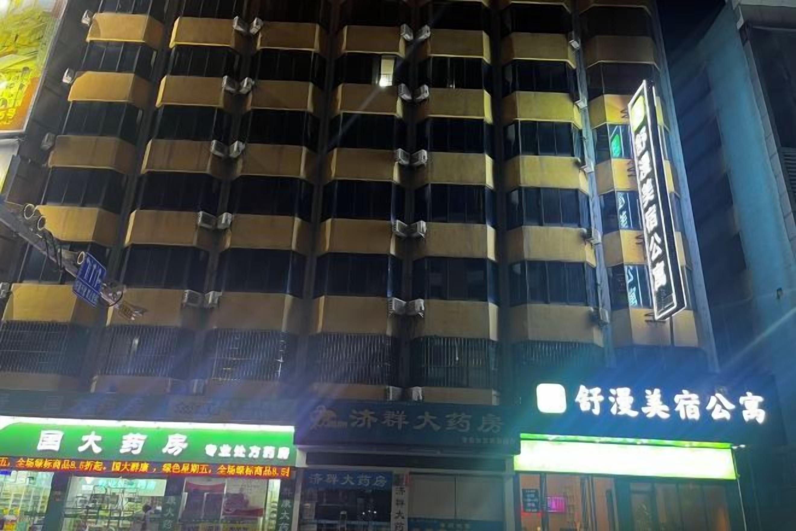 Un edificio de varios pisos con una serie de balcones y unidades de aire acondicionado. Hay letreros iluminados con texto, indicando la presencia de negocios o servicios en la planta baja.