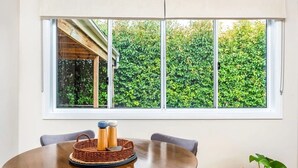 Een eetgedeelte met een ronde tafel, stoelen, een raam met uitzicht op groene beplanting en een kleine bloempot.