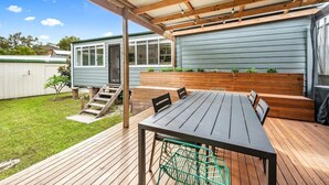 Een overdekt terras met een houten tafel en stoelen, een groene metalen stoel en een houten bank.