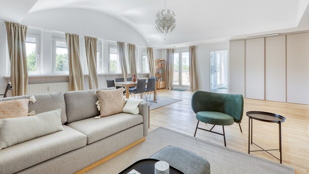 Ein geräumiges Wohnzimmer mit einer Couch, einem Sessel, einem Esstisch und einer Kandelaber.