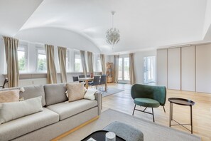 A spacious living room with a sofa, a chair, a dining table, and a chandelier.
