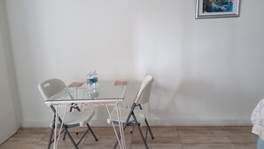Une petite pièce avec une table en verre et deux chaises, un tableau encadré au mur et un sol carrelé.