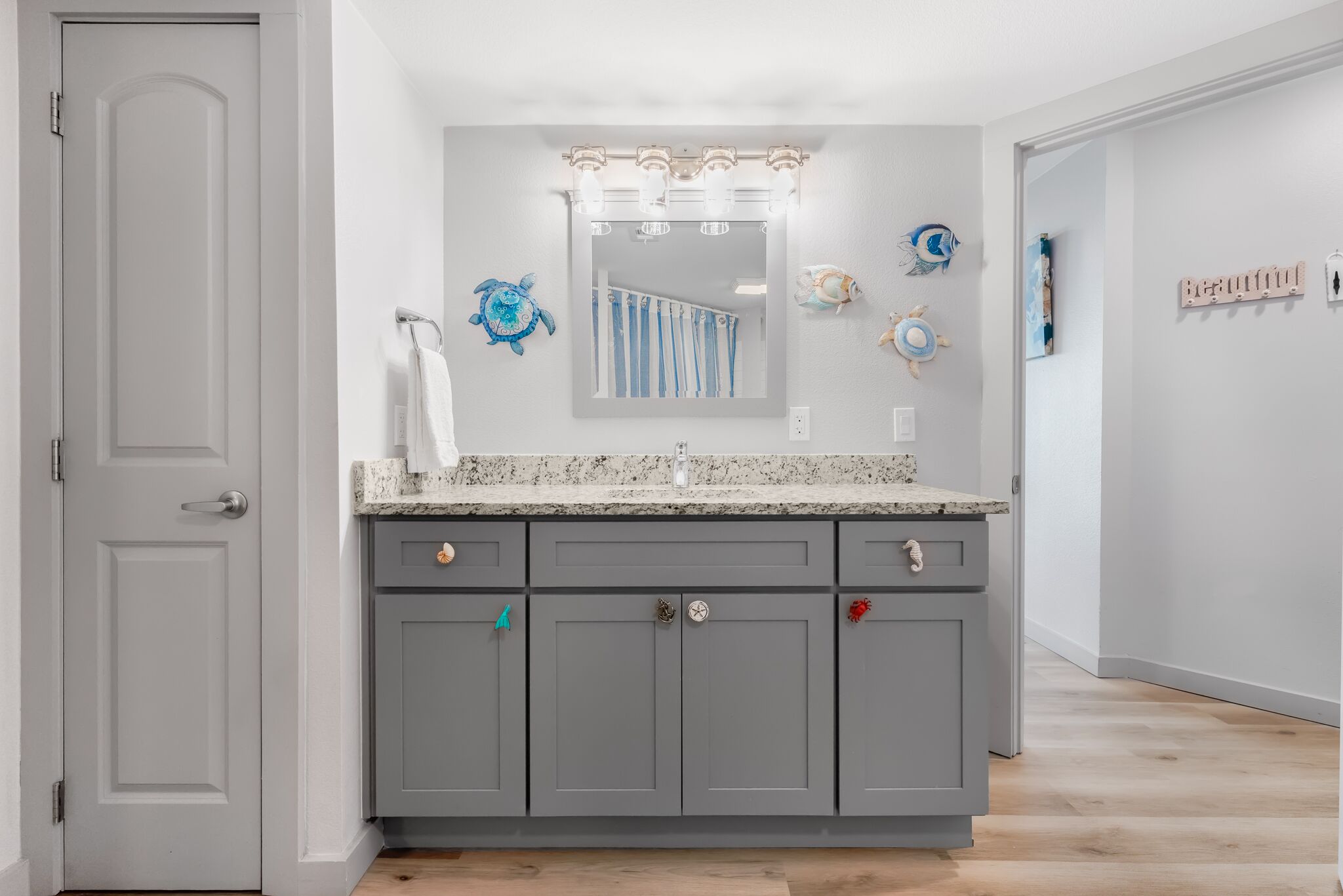 A bathroom with a grey vanity, a large mirror, and decorative wall art.