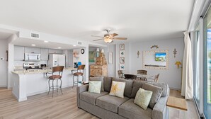 A modern kitchen with white cabinets, a central island, and bar stools. - Sandcastle Condominiums Unit 104 (Port Aransas)