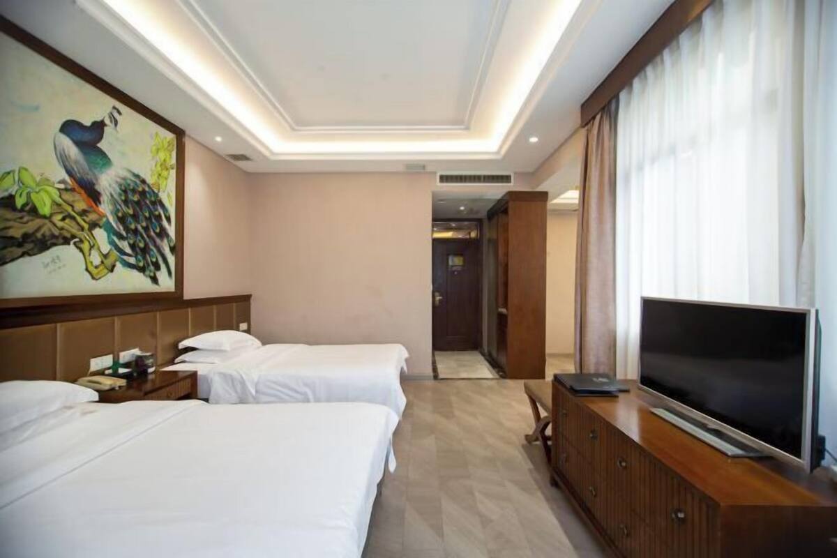 Hotellihuone, jossa on kaksi sänkyä, televisio ja taulu seinällä.