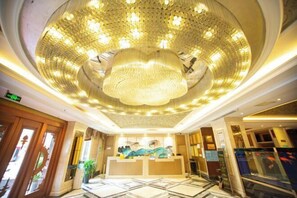 Een hotel lobby met een grote kroonluchter, receptiebalie en een vissenkom.