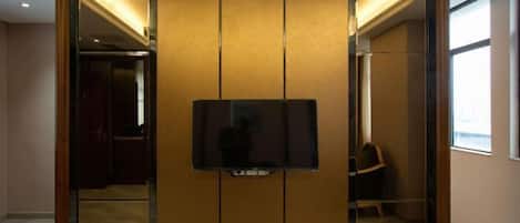 A room with a large mirror, a television mounted on a wooden panel wall, and a chair in the background.