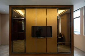 Una habitación con un espejo grande, un televisor instalado en una pared de paneles de madera, y una silla al fondo.