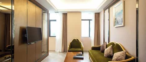 A modern hotel room with a green sofa, a wooden coffee table, and a television on a sliding door.