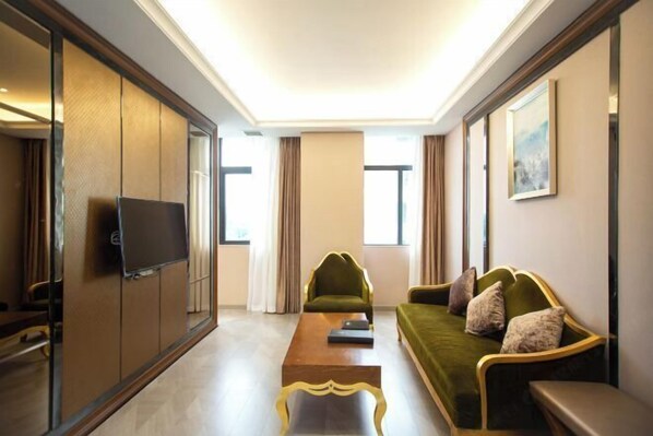 Una habitación de hotel moderna con un sofá verde, una mesa de centro de madera y un televisor en una puerta corredera.