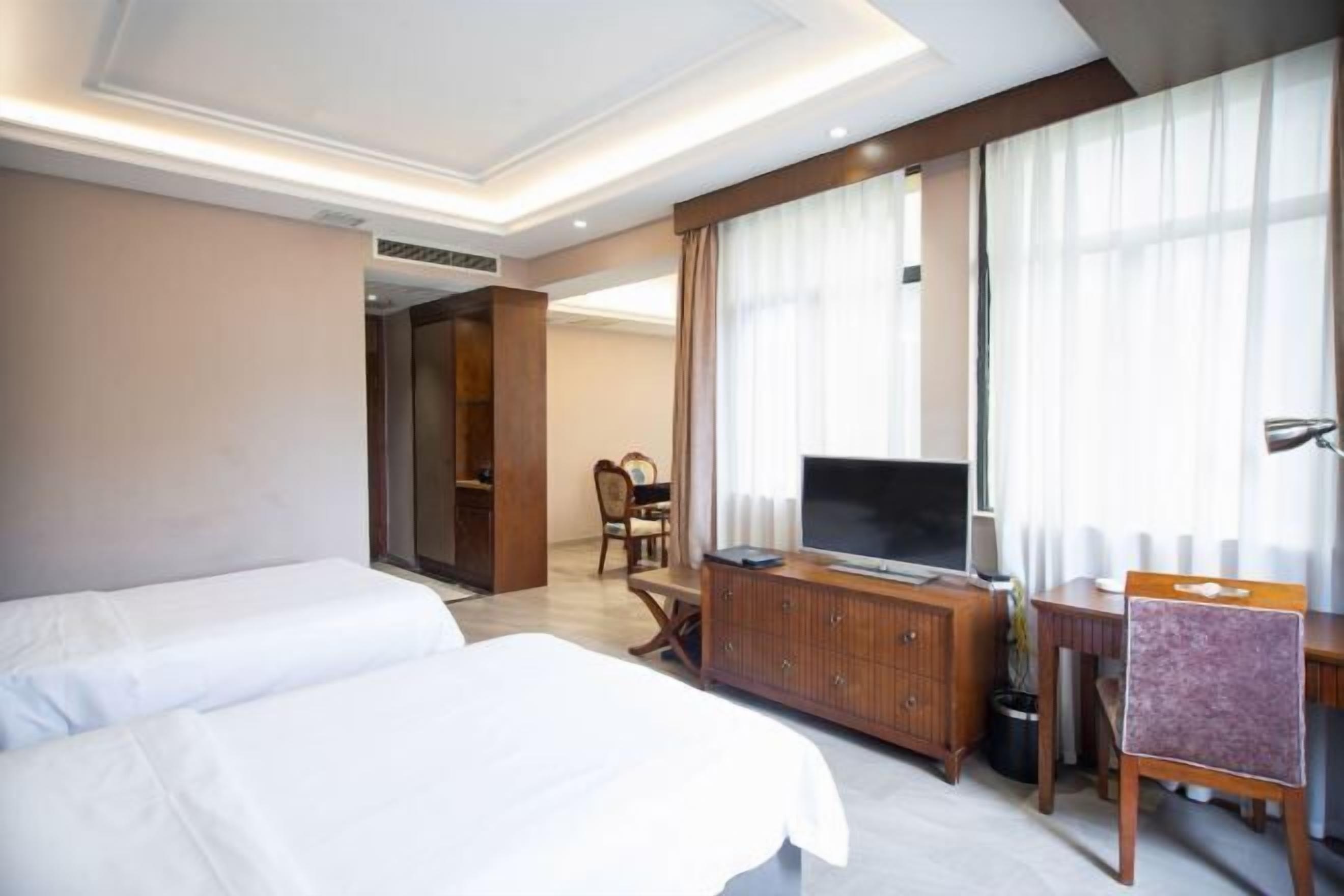 Quarto de hotel com duas camas, uma televisão, uma escrivaninha e uma cadeira.