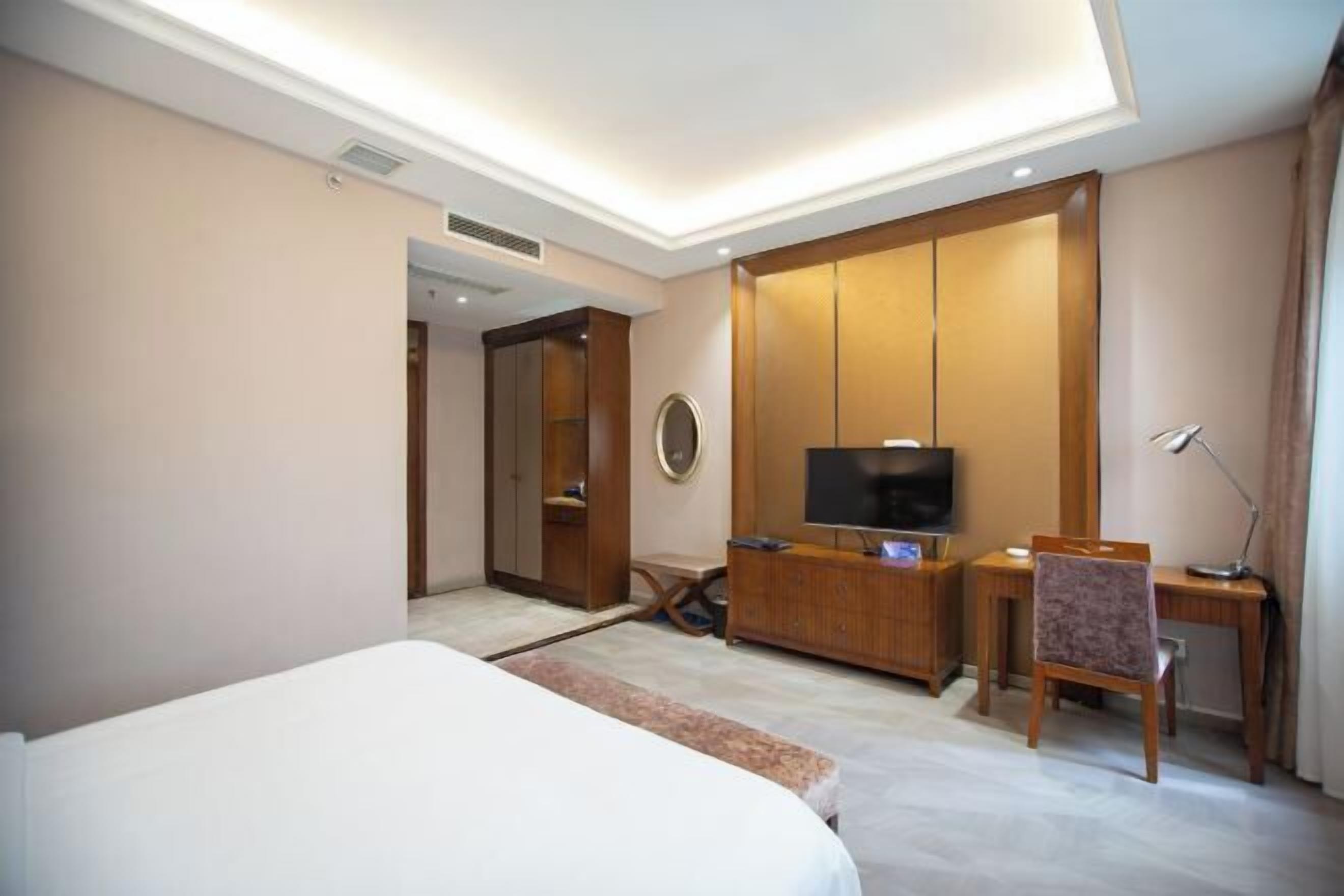 A hotel room with a bed, a desk, a television, and a wardrobe.