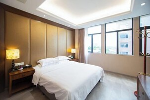 Habitación de hotel con una cama grande, dos mesitas de noche con lámparas, un armario y vistas a la ciudad a través de amplias ventanas.