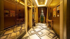 Een hotelgang met een vloer met geometrisch patroon, een potplant en een kleine tafel.