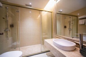 Un baño moderno con ducha de vidrio, lavamanos blanco y un espejo grande.